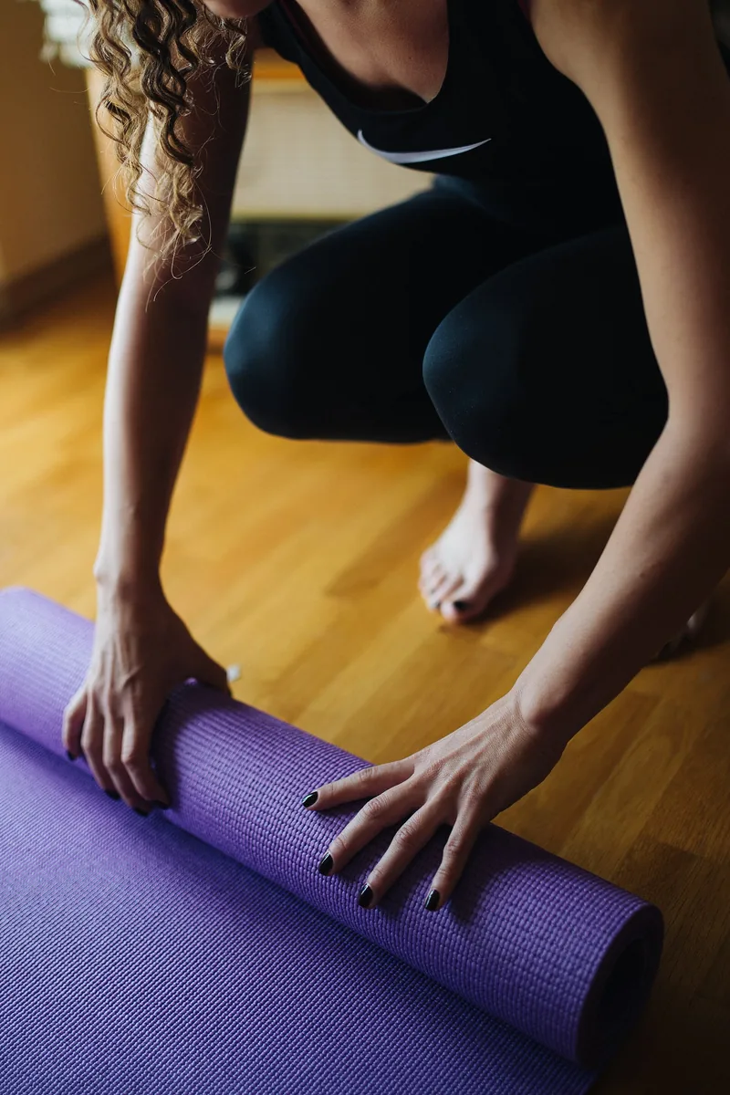 Hands rolling out a purple yoga mat on a wooden floor