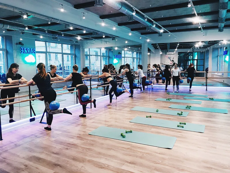 A barre class at a mirrored studio, with students at the rails and mats on the floor