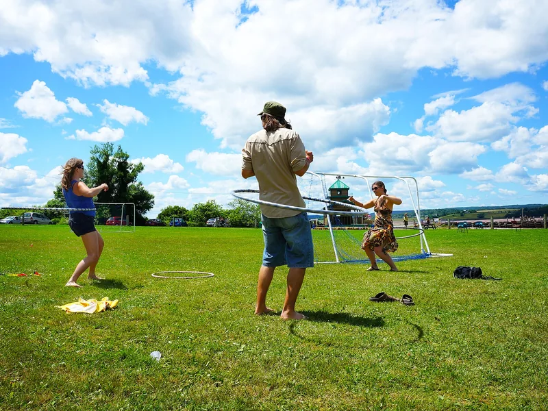 Three people hooping with large hoops on a grass field under a blue sky